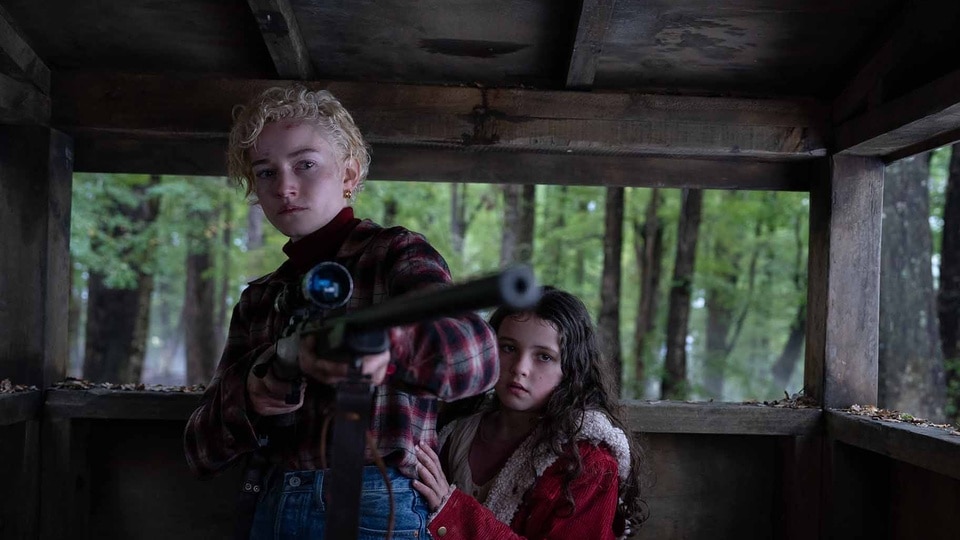 Charlotte (Julia Garner) holds a gun as Ginger (Matilda Firth) hangs on her in Wolf Man (2024).