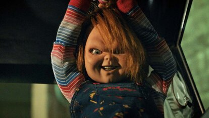 Chucky smiles murderously while holding a weapon above his head in Chucky 303.