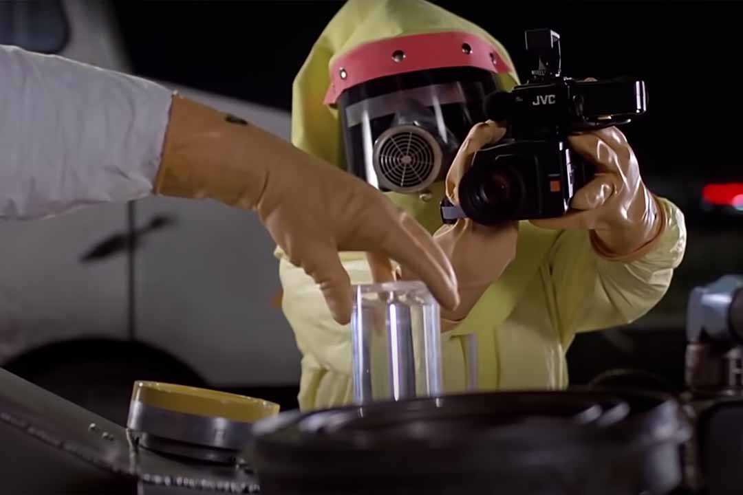 A hand holds a glass tube while a person in a protective suit points a camera at the hand in Back to the Future (1985).
