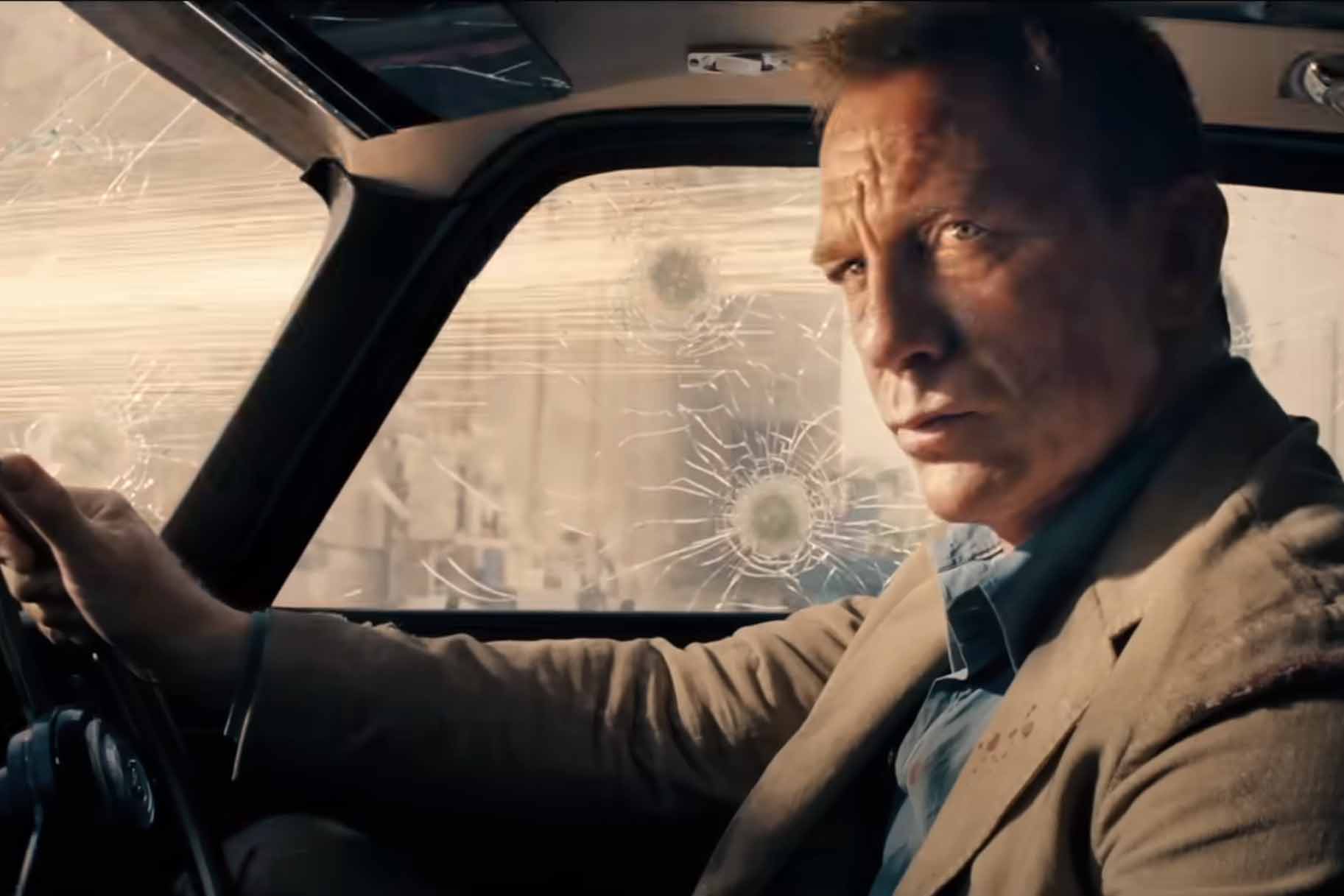 James Bond (Daniel Craig) drives a car with bullet holes in No Time to Die (2021).