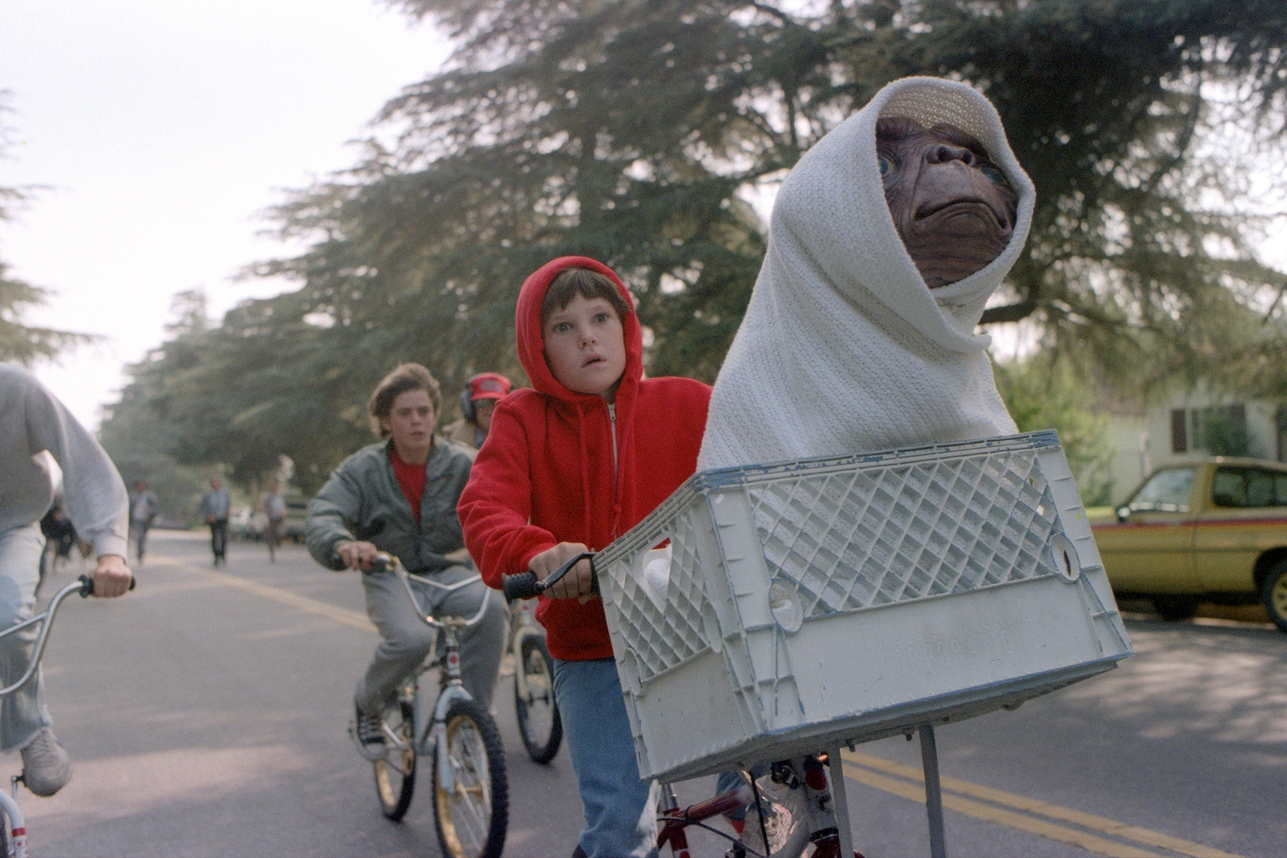 Elliott (Henry Thomas) rides a bike with E.T. wrapped in a blanket sitting in the basket in E.T. the Extra-Terrestrial (1982).