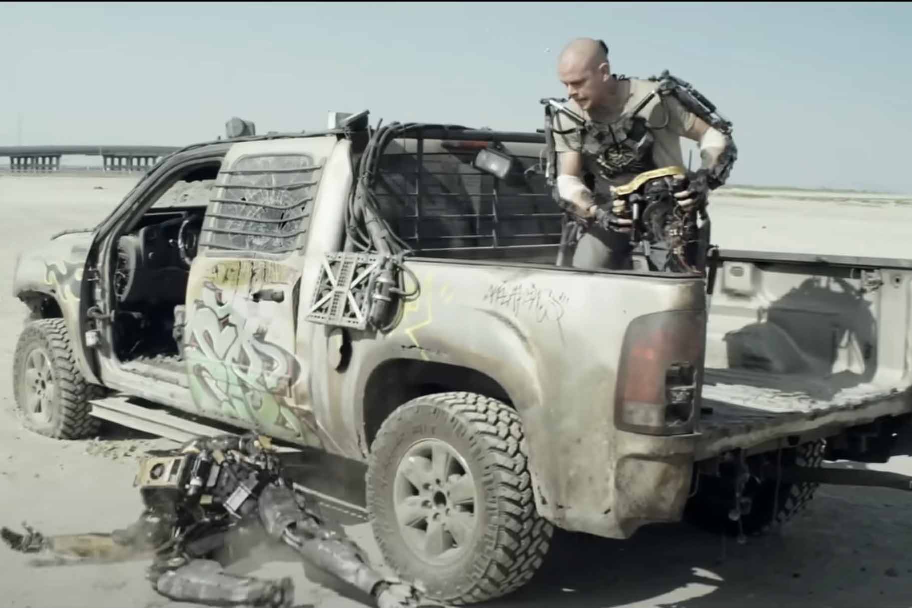 Max DeCosta (Matt Damon) stands in a tuck bed and looks at a decapitated robot in Elysium (2013).
