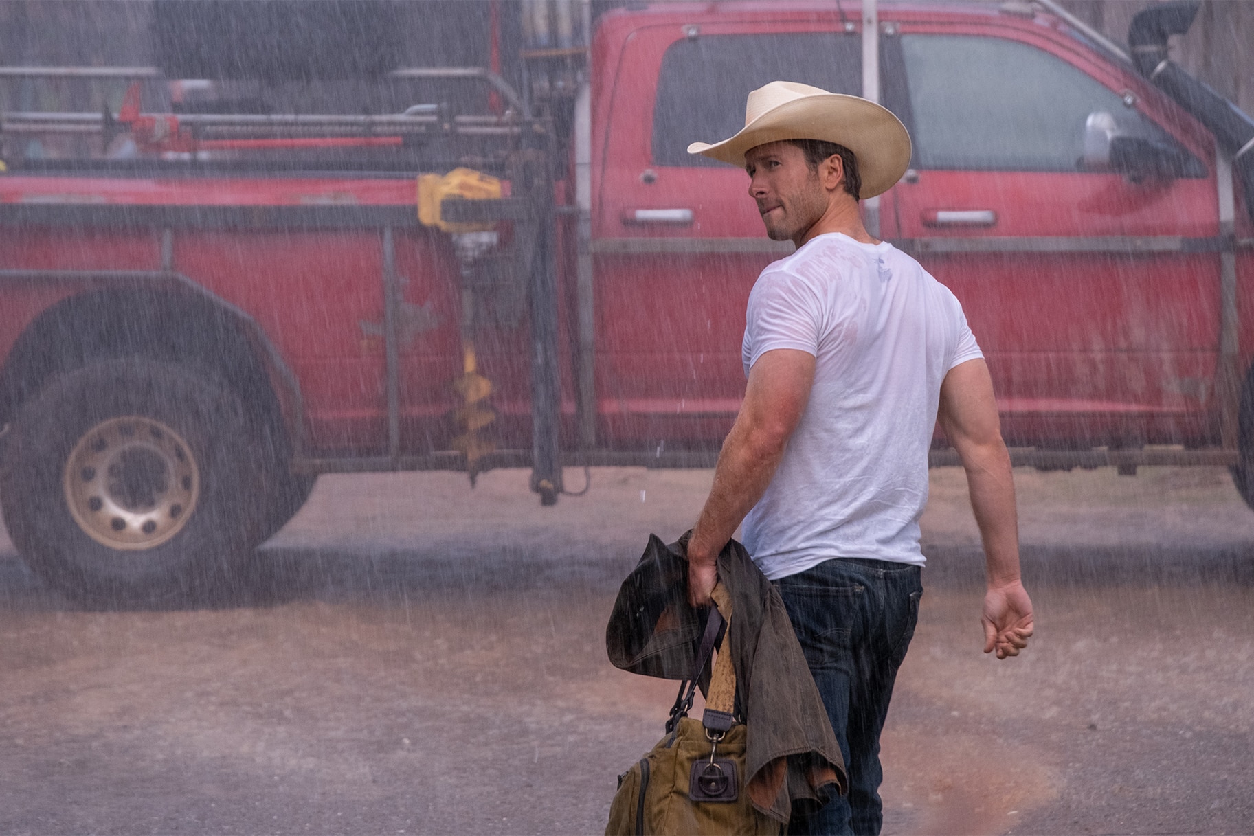 Tyler walks in the rain wearing a white t shirt and a cowboy hat