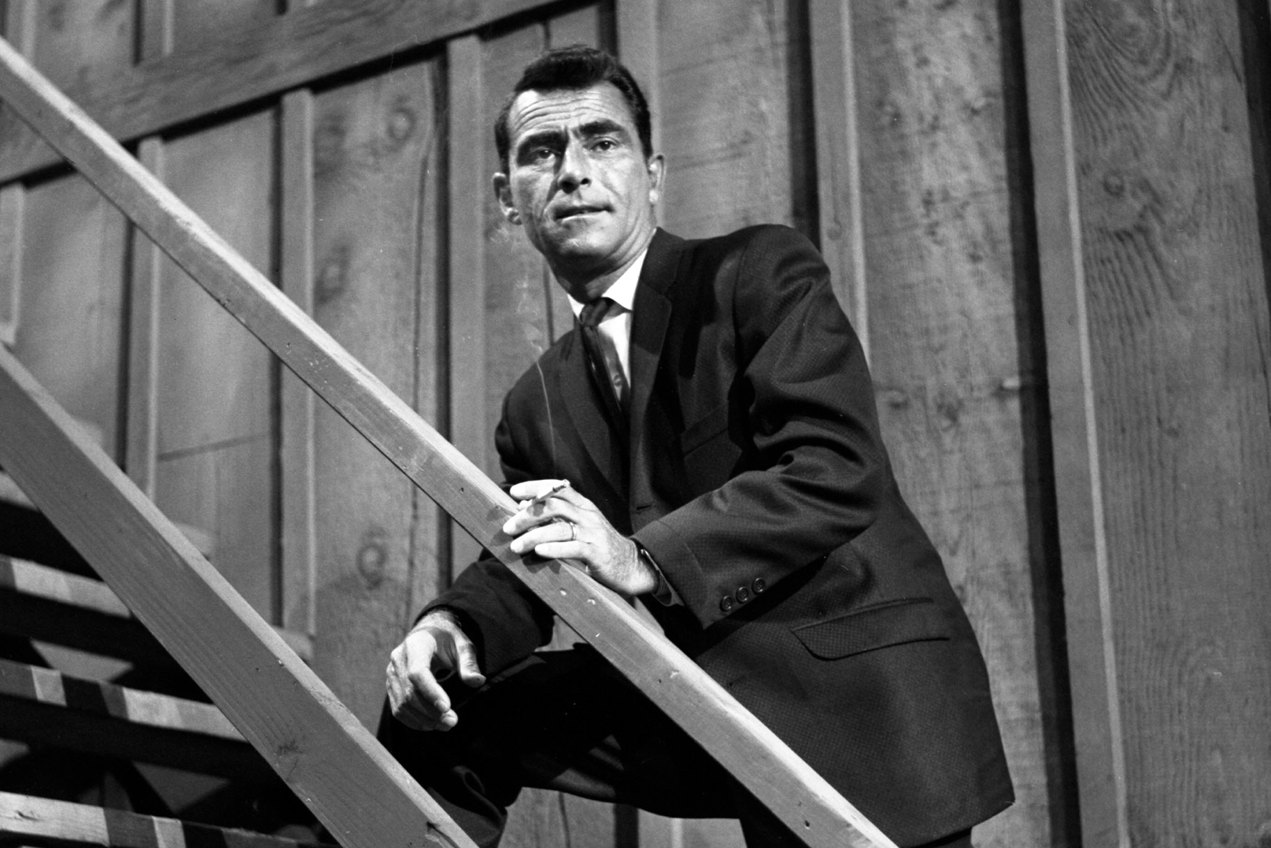 Rod Serling leans on a staircase railing on The Loner.