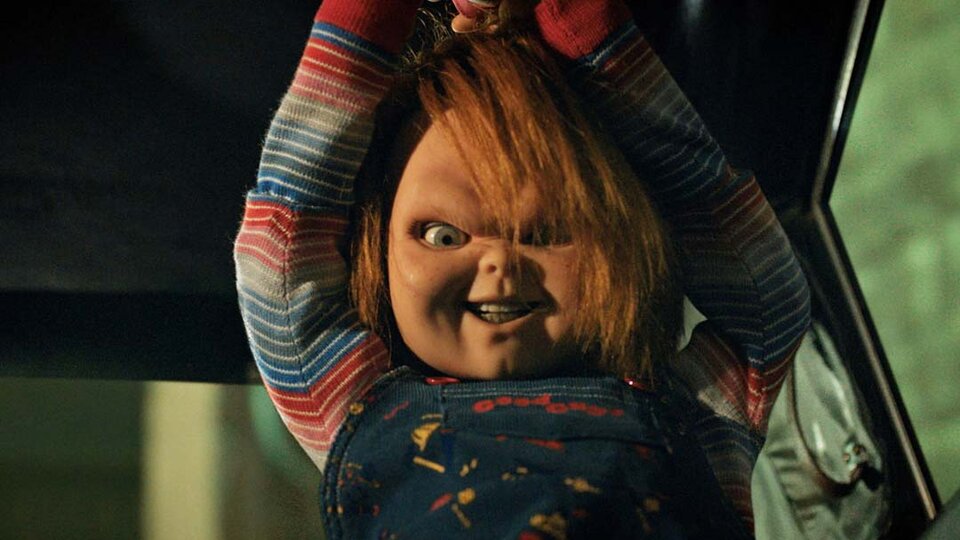 Chucky smiles murderously while holding a weapon above his head in Chucky 303.