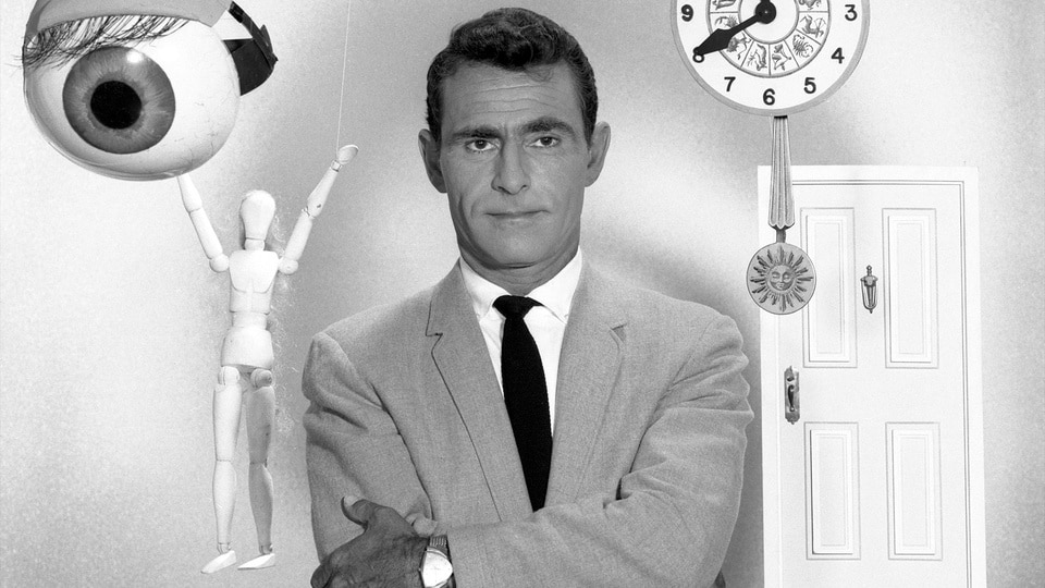 Rod Serling stands while an eye, a figurine, clock, and door float around him.