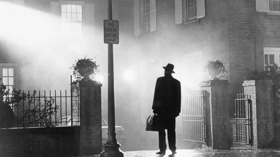 Father Merrin (Max von Sydow) stands outside under a streetlight in The Exorcist (1973).