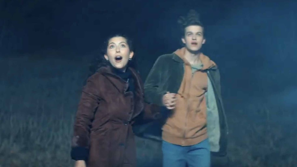 Itsy Levan (Emma Tremblay) and Calvin Kipler (Jacob Buster) look up at a bright object in the air in Aliens Abducted My Parents And Now I Feel Kinda Left Out (2023).