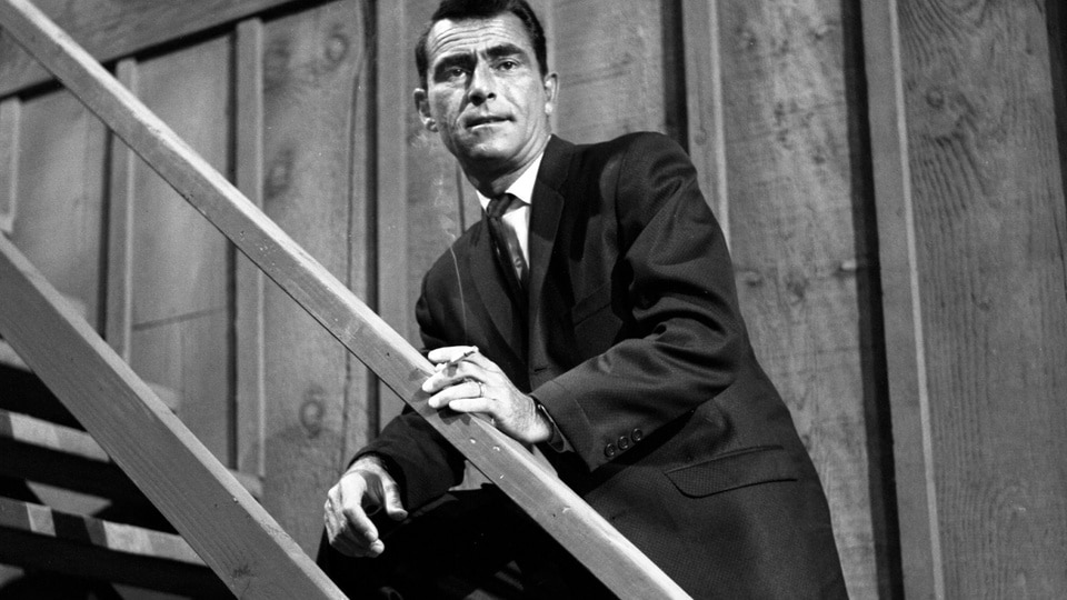 Rod Serling leans on a staircase railing on The Loner.