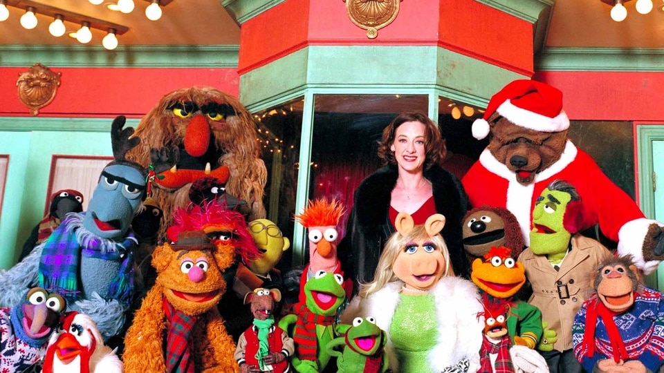 Joan Cusack smiles with the festively dressed Muppets in It's a Very Merry Muppet Christmas Movie (2002).