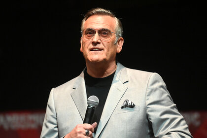 Bruce Campbell holds a microphone on stage during the 2022 Fandemic Tour