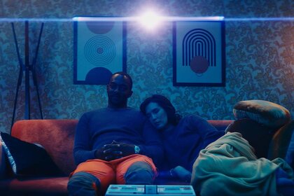 Adam (Anthony Mackie) and Jane (Zoë Chao) cuddle together on an orange couch in If You Were The Last (2023).
