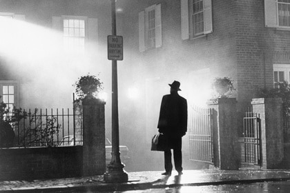 Father Merrin (Max von Sydow) stands outside under a streetlight in The Exorcist (1973).