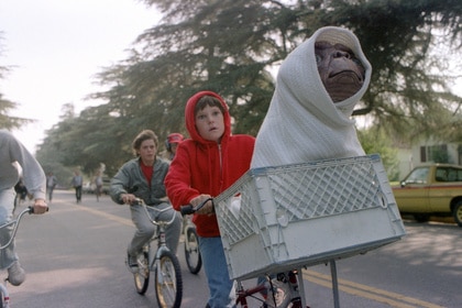 Elliott (Henry Thomas) rides a bike with E.T. wrapped in a blanket sitting in the basket in E.T. the Extra-Terrestrial (1982).