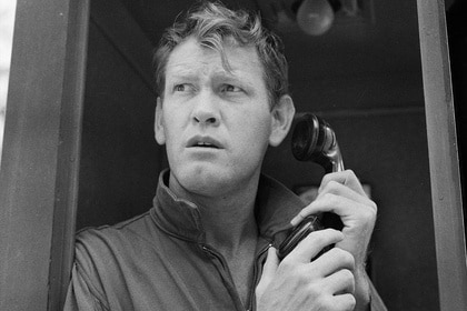 Earl Holliman holds a phone near him in a booth.