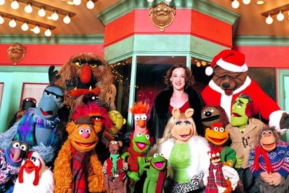 Joan Cusack smiles with the festively dressed Muppets in It's a Very Merry Muppet Christmas Movie (2002).