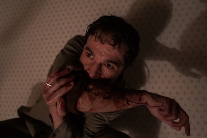 Blake (Christopher Abbott) sucks blood out of his wounded arm in Wolf Man (2025).