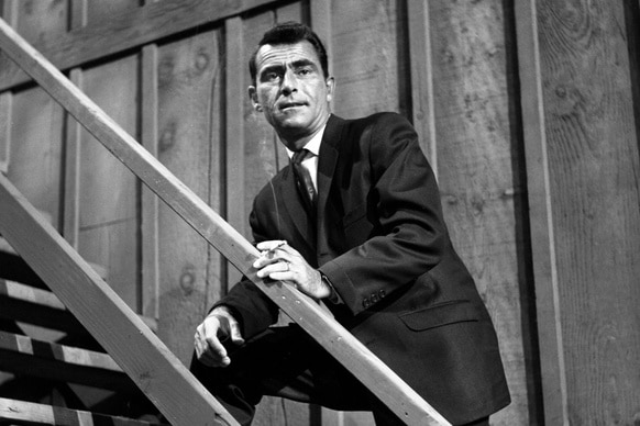 Rod Serling leans on a staircase railing on The Loner.