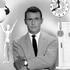 Rod Serling stands while an eye, a figurine, clock, and door float around him.