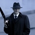 Sam Adama (Sasha Roiz) holds a gun while wearing a hat, glasses, and trench coat.