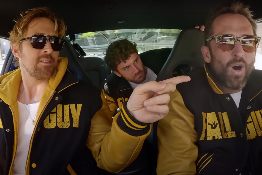 Ryan Gosling and his stuntmen wear matching The Fall Guy (2024) letterman jackets in a car.