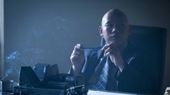 Reginald Andres sits at a desk in a suit in Reginald The Vampire Episode 203.