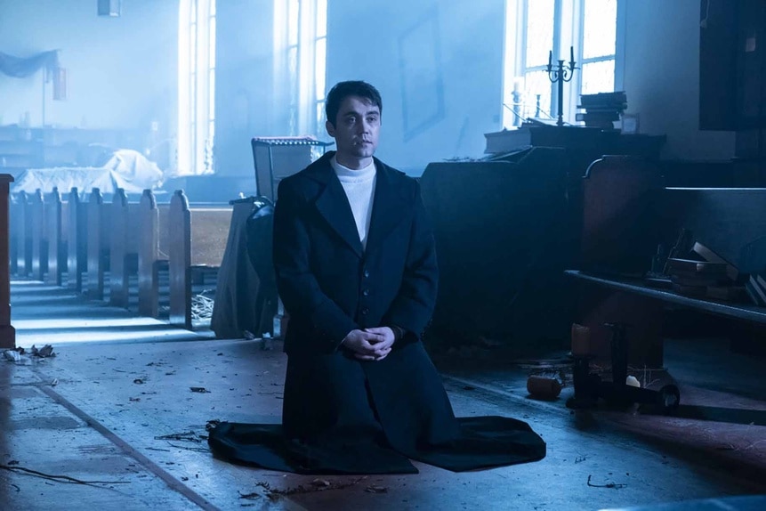 Uriel (Max Montesi) kneels in a church on Reginald the Vampire Episode 210.