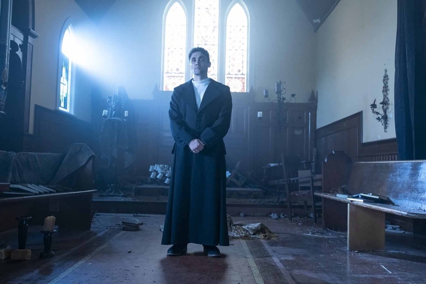 Uriel (Max Montesi) wears a black coat while standing at the front of a church on Reginald the Vampire Episode 210.