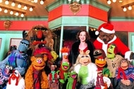 Joan Cusack smiles with the festively dressed Muppets in It's a Very Merry Muppet Christmas Movie (2002).