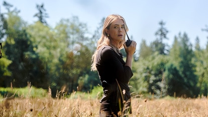 Rebecca Henderson walks in a field with a walkie talkie on The Hunting Party Season 1 Episode 3.