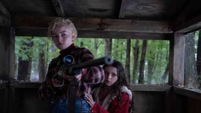 Charlotte (Julia Garner) holds a gun as Ginger (Matilda Firth) hangs on her in Wolf Man (2024).