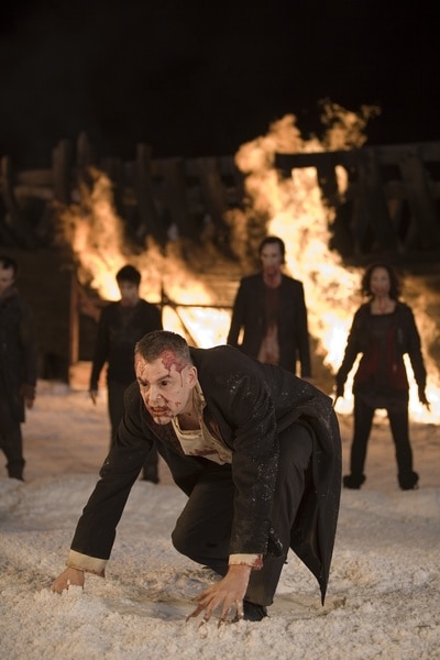 A bloody vampire crawls through snow with a large fire in the background in 30 Days of Night (2007).