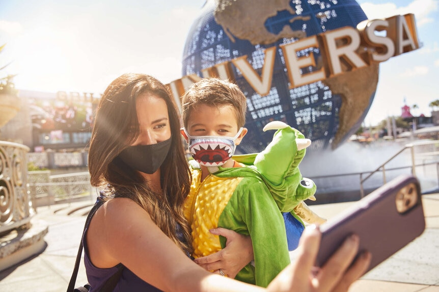 Woman and child in masks in front of Universal globe