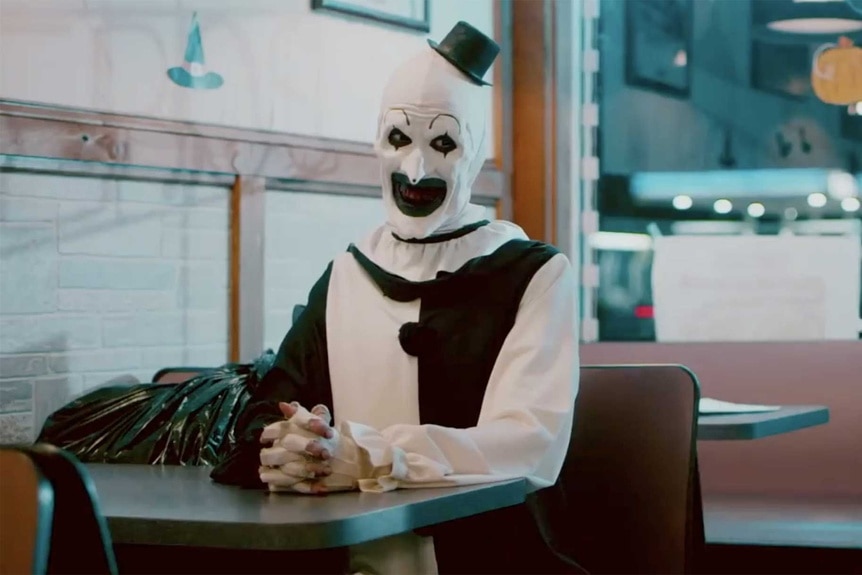 A scene of Art the Clown from Terrifier sitting in a pizza shop