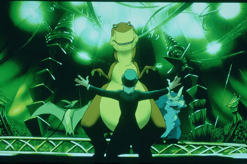 A circus trainer holds his arms out in front of three dinosaurs in We're Back! A Dinosaur's Story (1993).