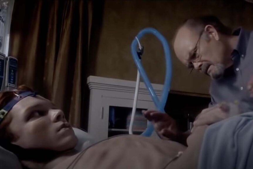 James (Cameron Monaghan) lays as Dr. Milton (Kurtwood Smith) tends to his injuries in Amityville: The Awakening (2017).