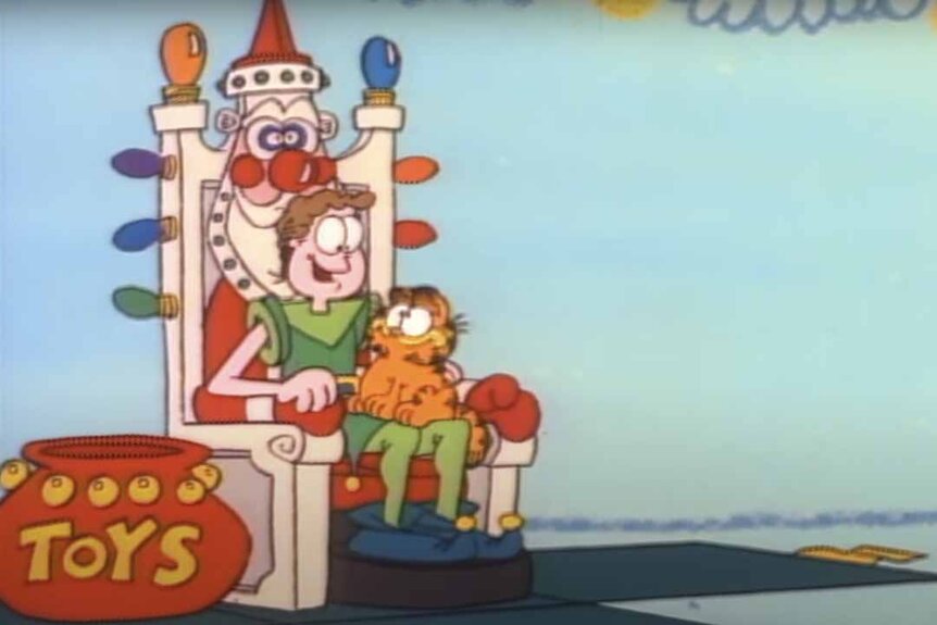 Garfield sits on Jon who sits on a mechanical Santa seat.