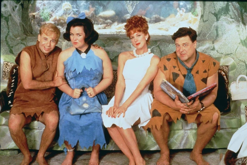Barney Rubble, Betty Rubble, Wilma Flintstone, and Fred Flintstone sit on a couch in The Flintstones (1994).