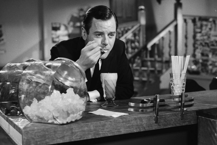 Martin Sloan (Gig Young) sits at a bar and eats a shake on The Twilight Zone.