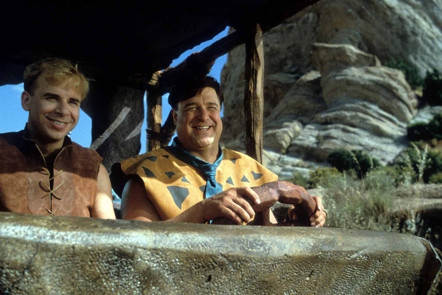 Barney Rubble (Rick Moranis) and Fred Flintstone (John Goodman) riding together in The Flintstones (1994).