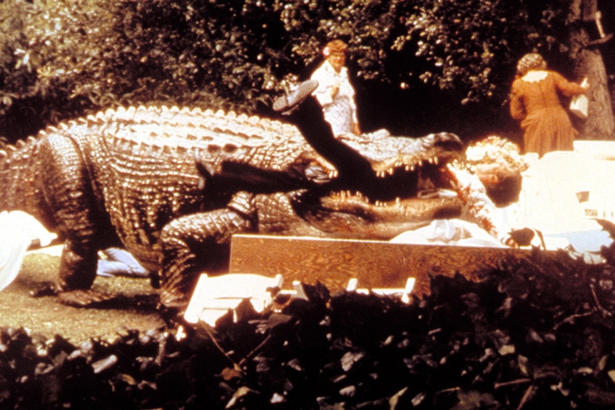 A still from the movie Alligator (1980) of a giant alligator eating a man with people behind it