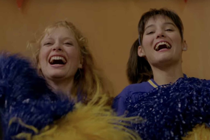 Colleen (Brenda James) and Paula Carson (Jill Schoelen) cheer with pom-poms in Cutting Class (1989).