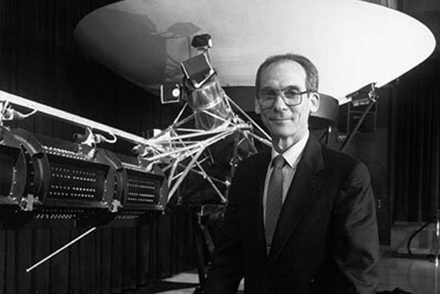 Ed Stone smiles in front of a model of the Voyager.