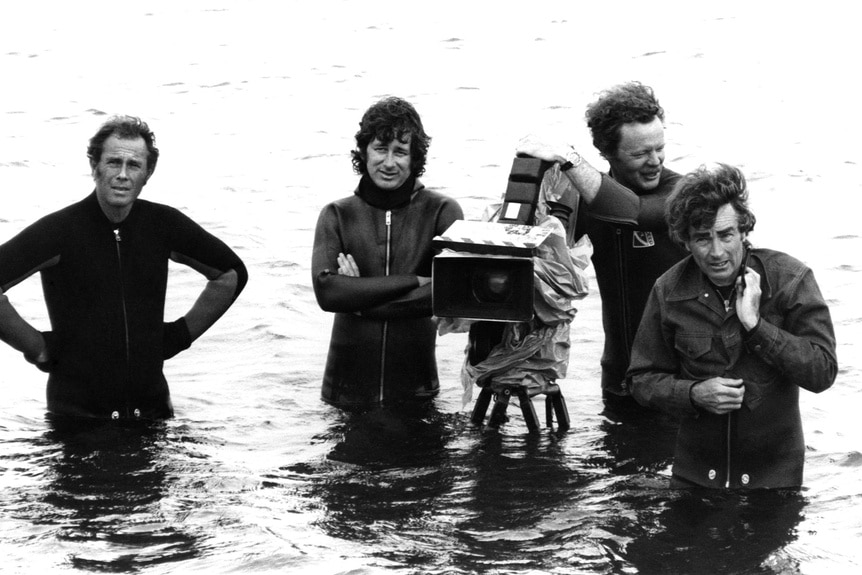 Steven Spielberg, Michael Chapman, and Bill Butler stand in water on the set of Jaws (1975).