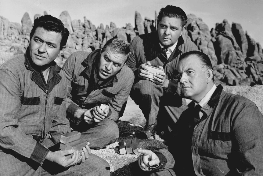 Four men gather gold bars in the desert.