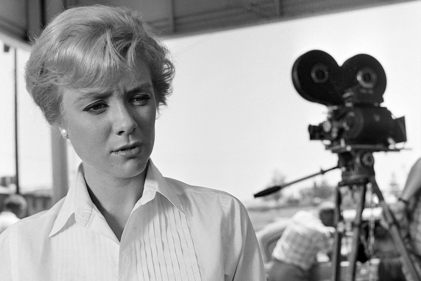 Nan Adams (Inger Stevens) stands with a film camera in the background in The Twilight Zone Episode 116.