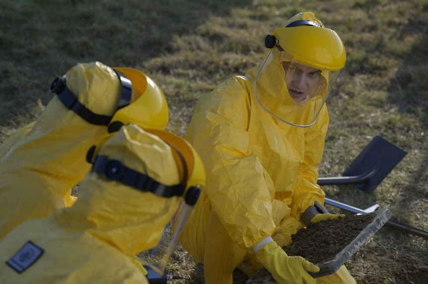 Angus Medford (Ryan Adams) wears a full-body protection suit and holds a dirt sample on The Ark Episode 212.