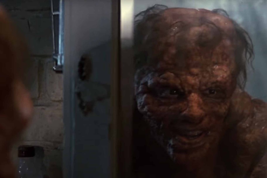 A mutated gross Seth Brundle (Jeff Goldblum) looks in the mirror in The Fly (1986).