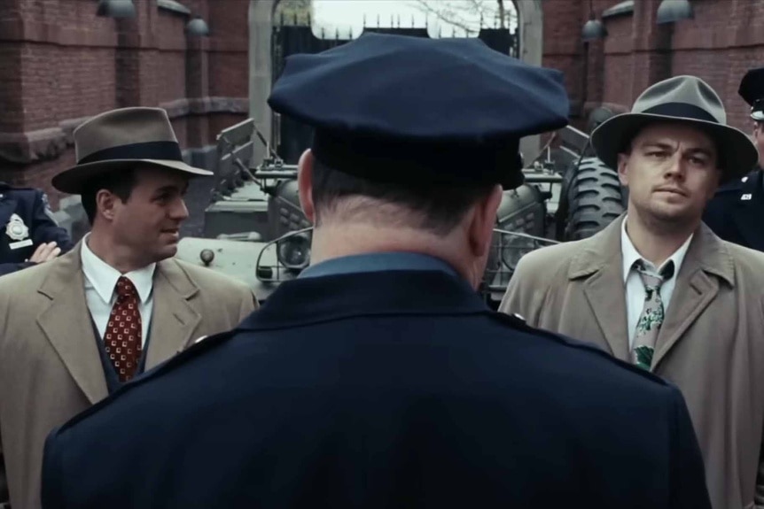 Chuck Aule (Mark Ruffalo) abd Teddy Daniels (Leonardo DiCaprio) wear trench coats and talk to a cop on Shutter Island (2010).