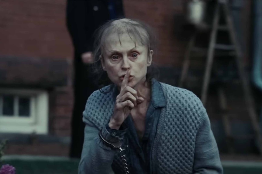 A disheveled lady does a shushing motion in Shutter Island (2010).